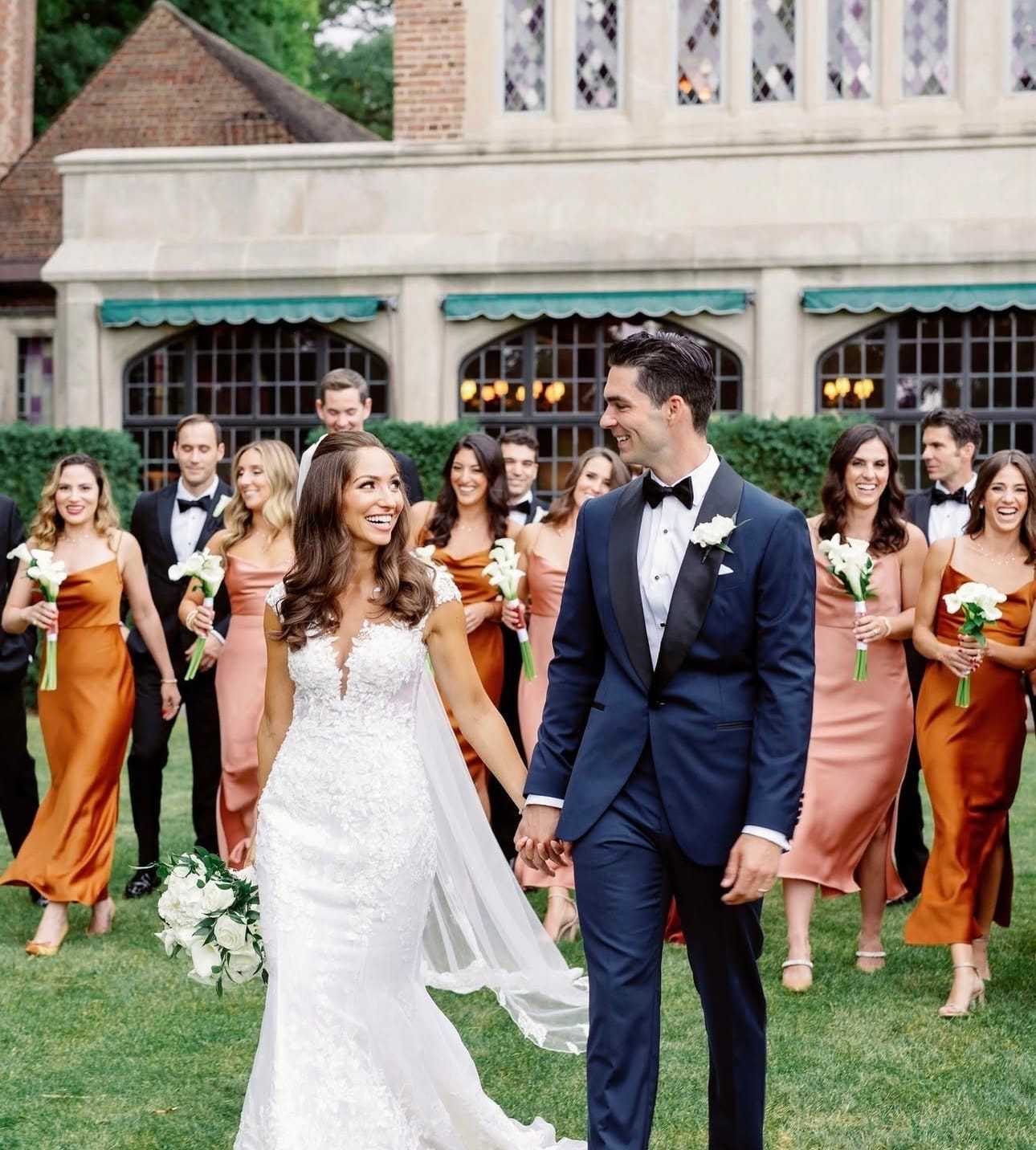 Wedding couple with bridesmaids and groomsmen smiling in elegant attire outside a building.